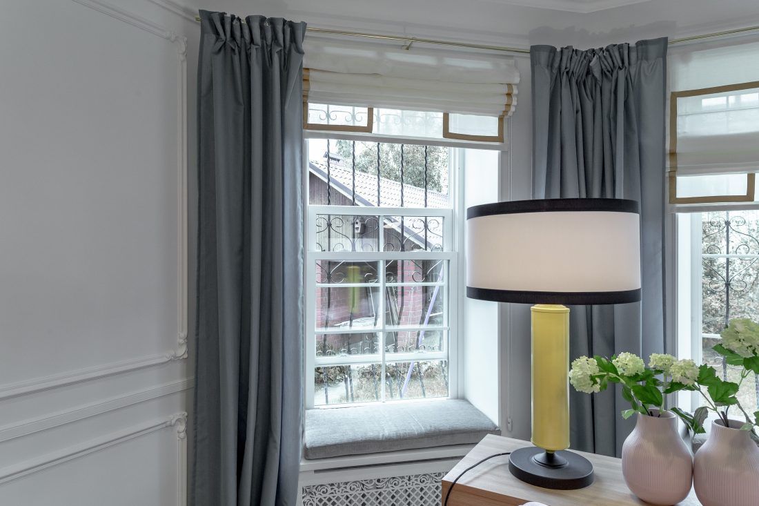 Оформление окна: римские шторы, легкие синие занавески и мягкие матрасики но подоконниках.