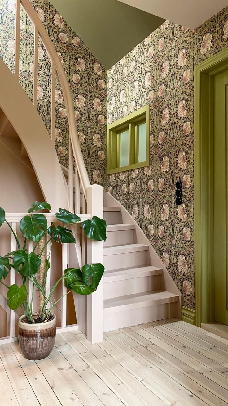 Гостиная в викторианском стиле в зелёно‑розовых тонах. У стены — тёмный резной камин, стены выкрашены в мягкий зелёный цвет и украшены картинами в золотых рамах. В центре стоит зелёный бархатный диван с розовыми и бежевыми подушками. Перед ним — низкий деревянный стол со стеклом и большим букетом ярко‑розовых пионов в прозрачной вазе. На заднем плане — ещё розовые цветы, свет в комнату идёт из высокого окна.