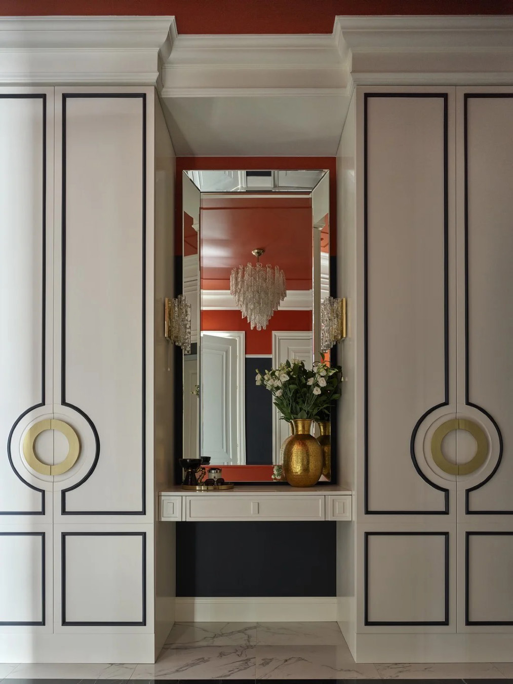 Прихожая с симметричными белыми шкафами с графичным чёрным декором, консолью с зеркалом по центру, красным потолком, мраморным полом и золотой вазой с цветами.