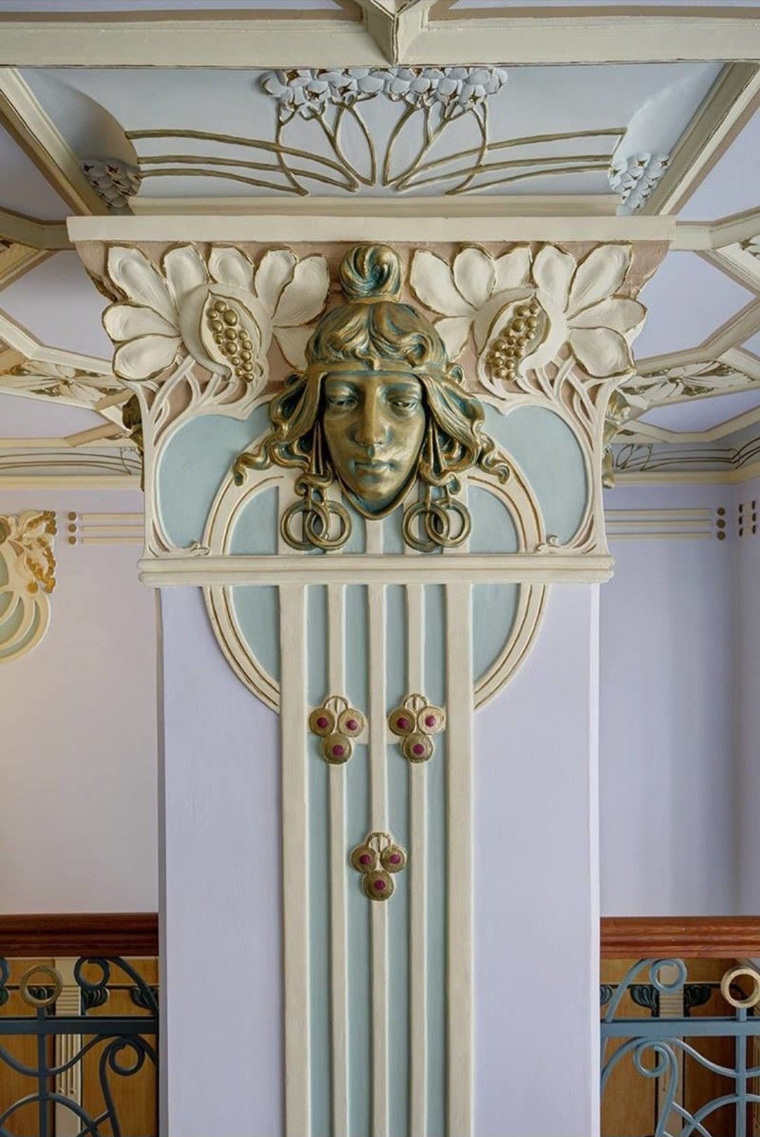 Интерьер в стиле модерн: колонна с маскароном, обрамлённым лепниной в виде цветов и листьев. Мягкие кремовые и мятно‑голубые тона, плавные линии и декоративный потолок создают характерную атмосферу начала XX века.