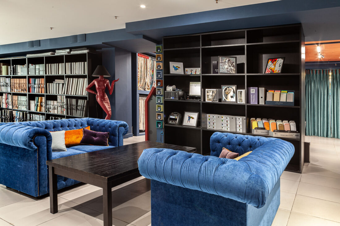 Интерьер дизайн‑центра Ампир Декор на Автозаводской с синими диванами, чёрными стеллажами с каталогами и образцами материалов и зоной для переговоров.