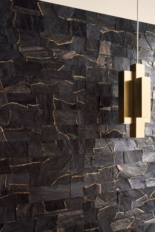 Стена, отделанная натуральным настенным покрытием из коры кокосовой пальмы с объёмной фактурой, рядом современный подвесной светильник геометричной формы.